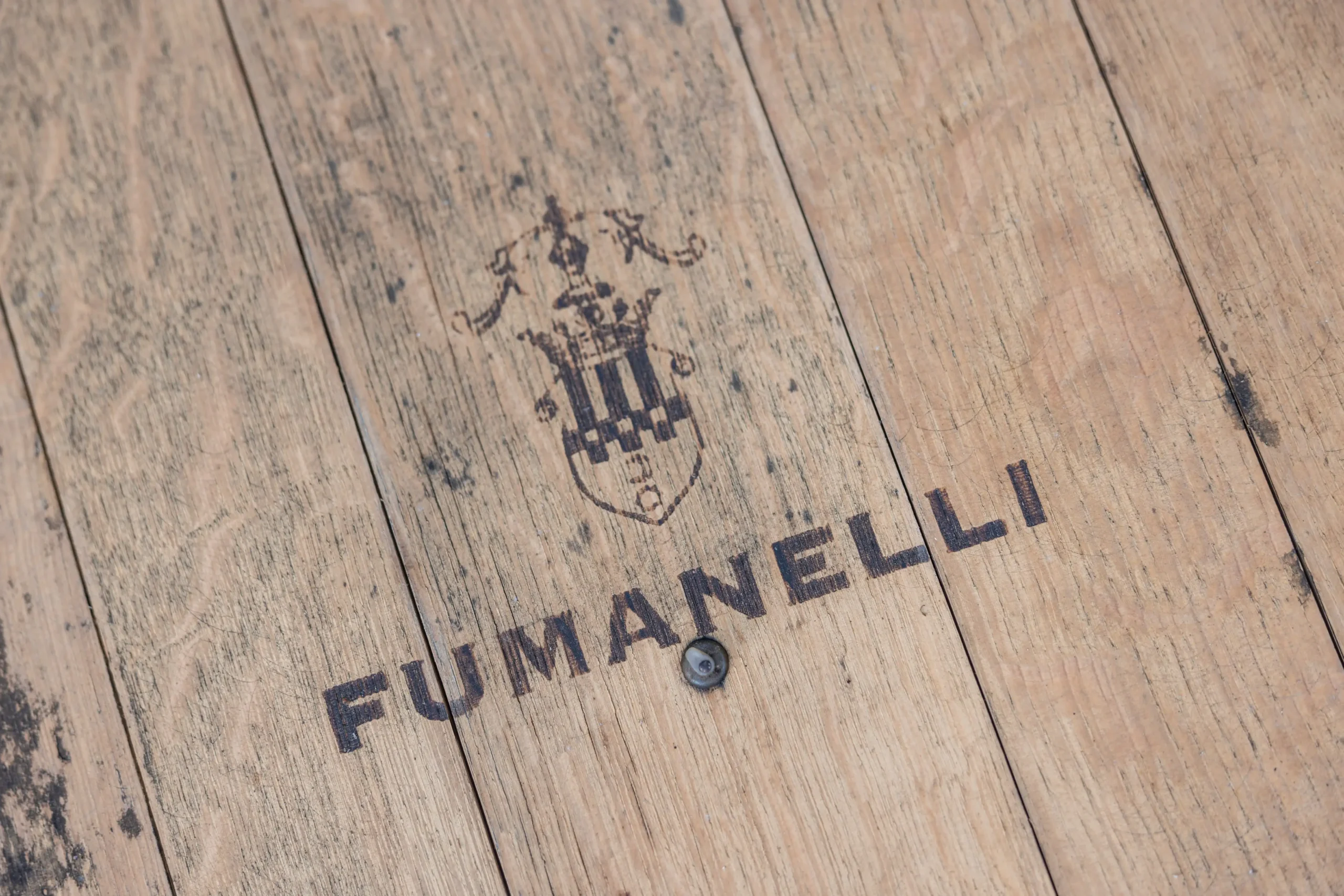 Logo Fumanelli inciso su botte in legno, dettaglio ravvicinato della superficie rustica.