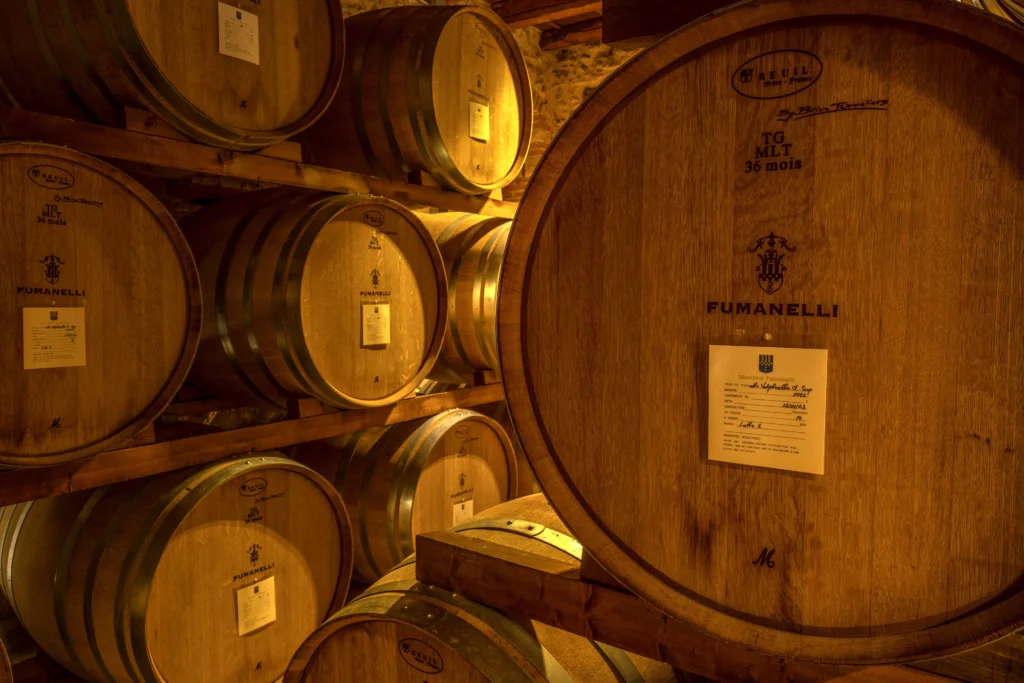 Botti di rovere Fumanelli nella cantina di affinamento, etichettate e ordinate su scaffalature in legno.