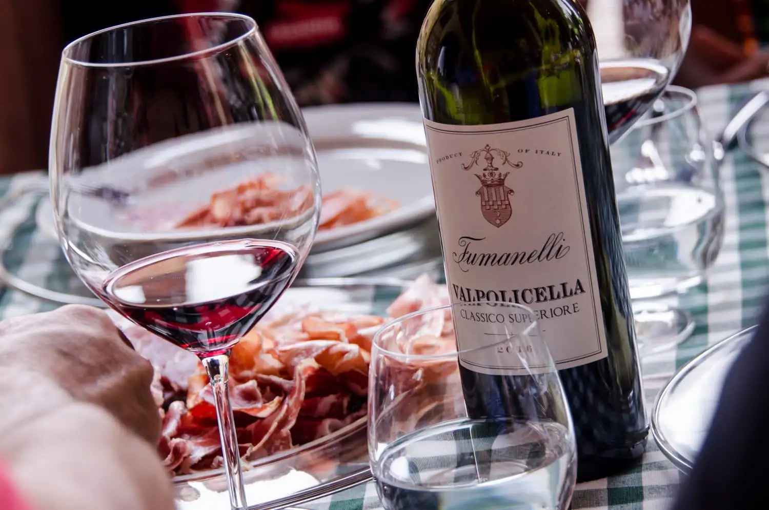 Bottiglia di Valpolicella Fumanelli con calice di vino rosso e tagliere di salumi in primo piano.