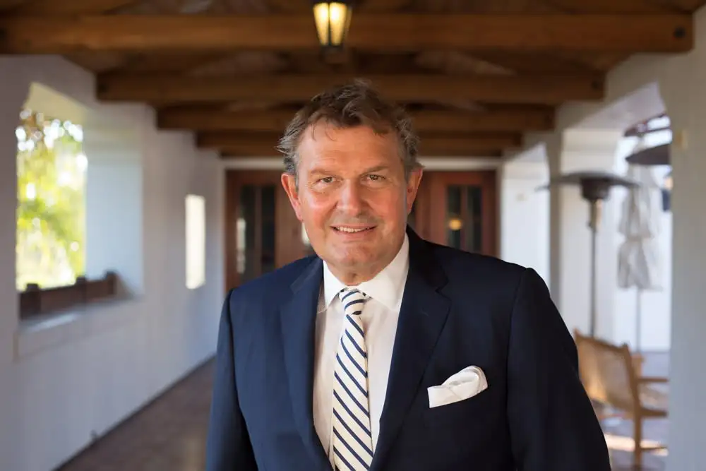 Ritratto di un uomo elegante in abito blu con cravatta a righe, in una location luminosa con soffitto in legno.