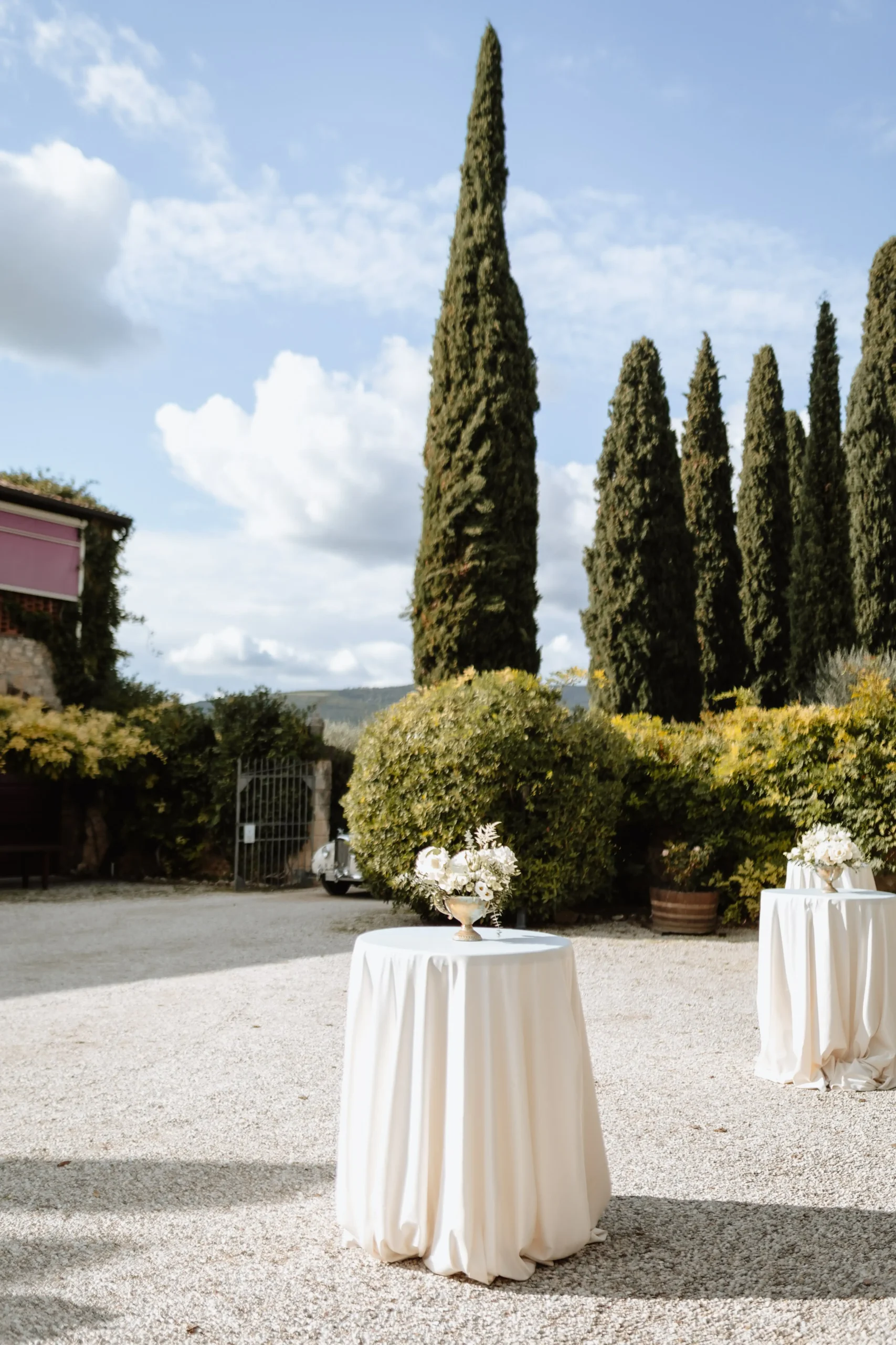 Tavolo elegante allestito per evento all’aperto presso la tenuta Fumanelli, con cipressi e vegetazione sullo sfondo.